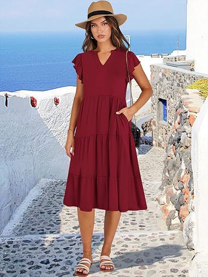 Woman in a red dress and hat standing on a picturesque Mediterranean street.
