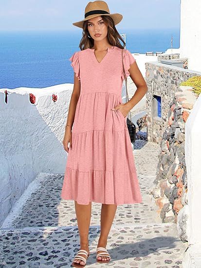 Woman in a pink dress and straw hat standing on a picturesque Mediterranean street.