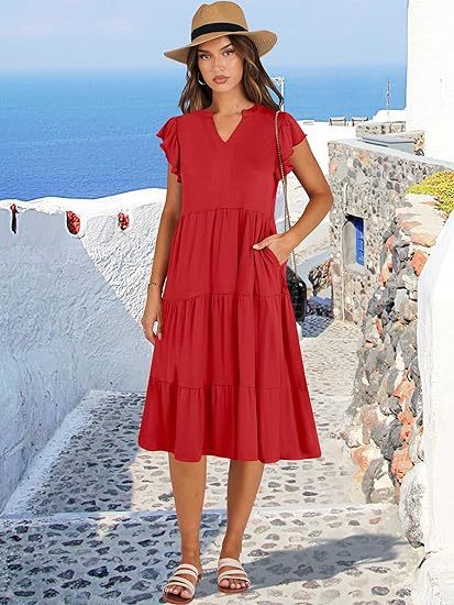 Woman in a red dress and hat standing on a picturesque Mediterranean street.