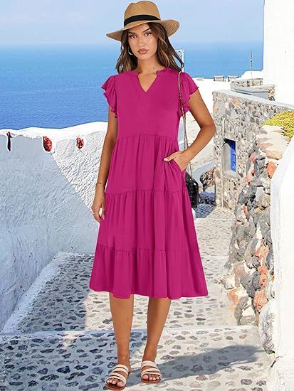 Woman in a pink dress and hat standing on a picturesque Mediterranean street.