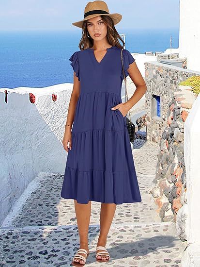 Woman in a blue dress and hat standing on a picturesque Mediterranean street.