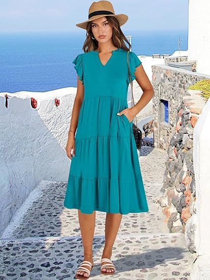 Woman in a teal dress and hat standing on a picturesque Mediterranean street.